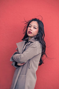 Portrait of confident woman with arms crossed standing against red wall