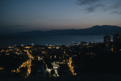 High angle view of illuminated buildings by sea against sky at sunset