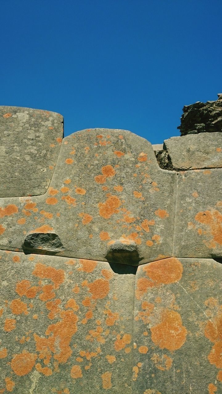 clear sky, blue, copy space, built structure, architecture, building exterior, low angle view, sunlight, wall - building feature, rock - object, outdoors, day, no people, nature, shadow, mountain, yellow, tranquility, stone wall, beauty in nature