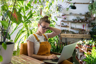 Woman using laptop while sitting amidst plants in workshop