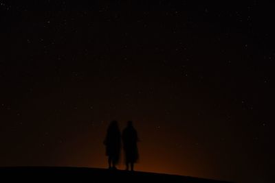 Rear view of silhouette woman standing against sky at night