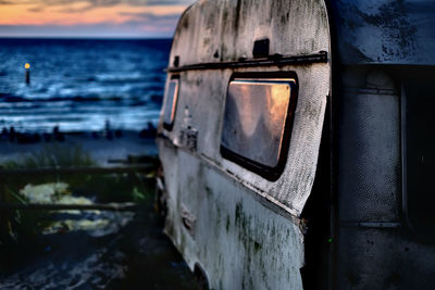 Abandoned boat at beach against sky during sunset