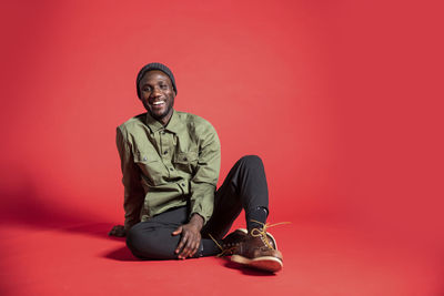 Portrait of young man sitting against red background