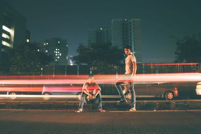 Long exposure of vehicles by people on road against sky at night