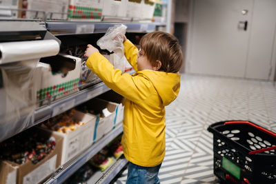 Child in the market with a grocery cart, puts sweets in a bag