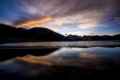 Scenic view of lake by mountains against sky during sunset