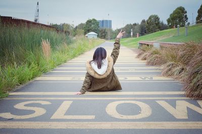 Rear view of woman showing peace sign while sitting on road