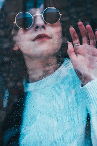 Woman wearing sunglasses seen though wet window
