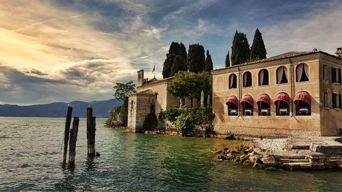 Old building by river against cloudy sky