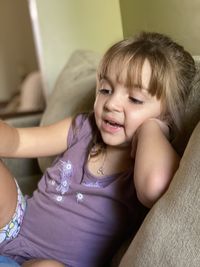 Close-up of smiling girl sitting on sofa at home