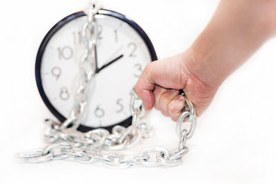 Close-up of hand holding clock against white background