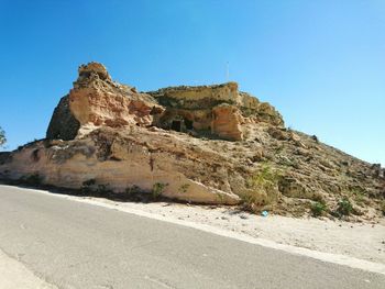 View of rock formation by road against clear blue sky