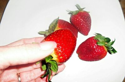 Close-up of cropped hand holding strawberry over white background