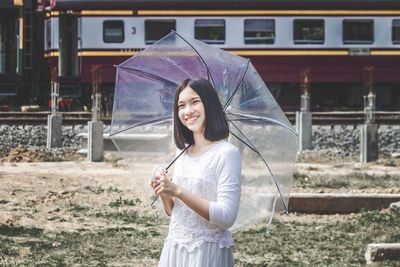 Portrait of smiling young beautiful women holding umbrella standing in front of train.