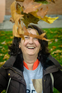 Portrait of smiling woman by autumn leaves in park