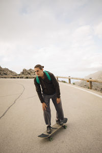 Young man skateboarding on road against sky during vacation