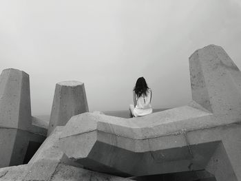 Rear view of woman sitting on tetrapods against sky