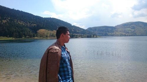 Young man standing by lake against sky