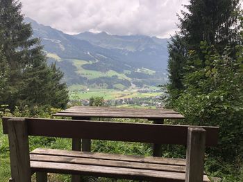 Bench by trees and mountains against sky