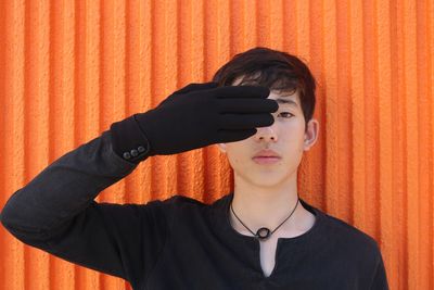 Portrait of young man wearing sunglasses standing against orange wall