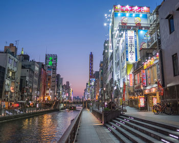 Canal amidst illuminated buildings in city during sunset