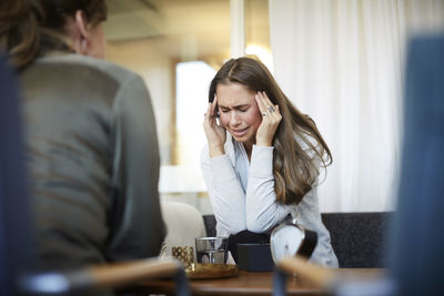 Stressed crying teenager with head in hands sharing problems with therapist at wellness center