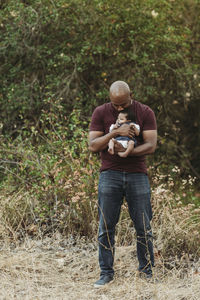 Portrait of happy father holding newborn age daughter in backlit field