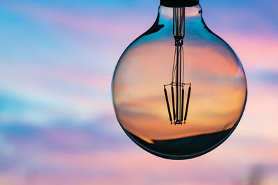 Close-up of light bulb against sky during sunset