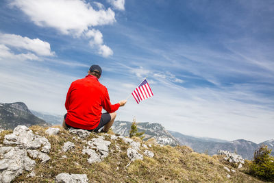 Rear view of person on rock in mountains against sky