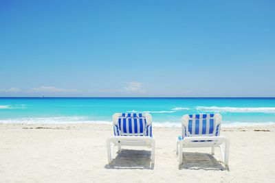 Deck chairs on beach against clear blue sky