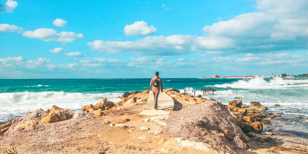 Man standing on rock at beach against sky