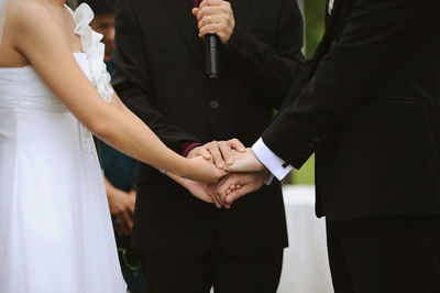 Midsection of priest holding hands of couple during weeding