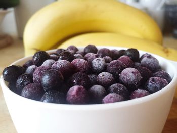 Close-up of black currants in bowl by bananas on table