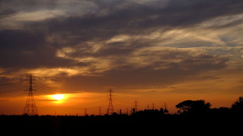 Silhouette electricity pylons on field against orange sky