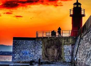 Man standing by lighthouse against sky during sunset