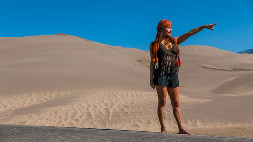Rear view of young woman standing in desert against clear blue sky