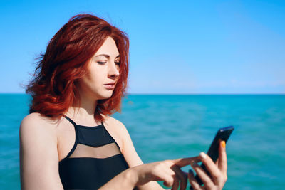 Portrait of young woman using mobile phone against sea