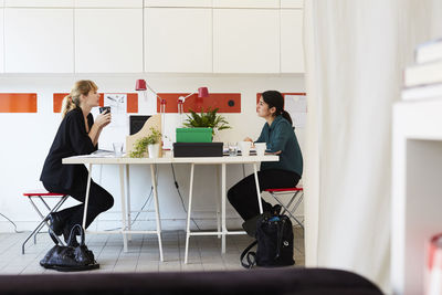 Side view of mid adult businesswoman talking at table in office