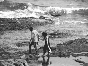 Couple holding hands while walking at shore of beach