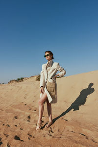 Side view of young woman standing at beach against clear sky