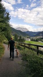 Rear view of man walking with dog on footpath