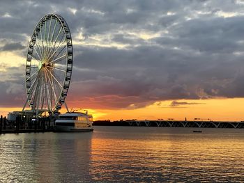 Ferris wheel by sea against sky during sunset