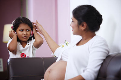 Girl listening music with pregnant mother while sitting on sofa at home