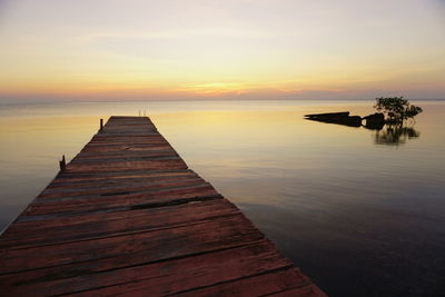 Wooden pier over sea against sky during sunset