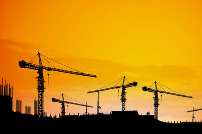 Silhouette cranes at construction site against sky during sunset