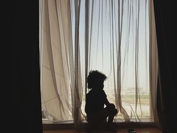 Silhouette boy looking through window at home