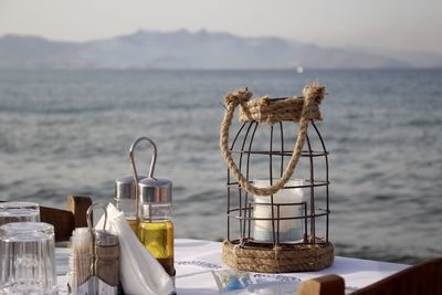 Lantern by olive oil in container on table against sea