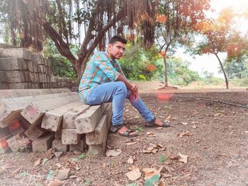 Side view of young man sitting on tree