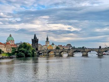 Arch bridge over river by buildings against sky in city
