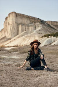 Portrait of young woman sitting on rock against sky